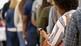 En mangfoldig gruppe mennesker som tålmodig venter i kø, fokusert på mobiltelefonene sine