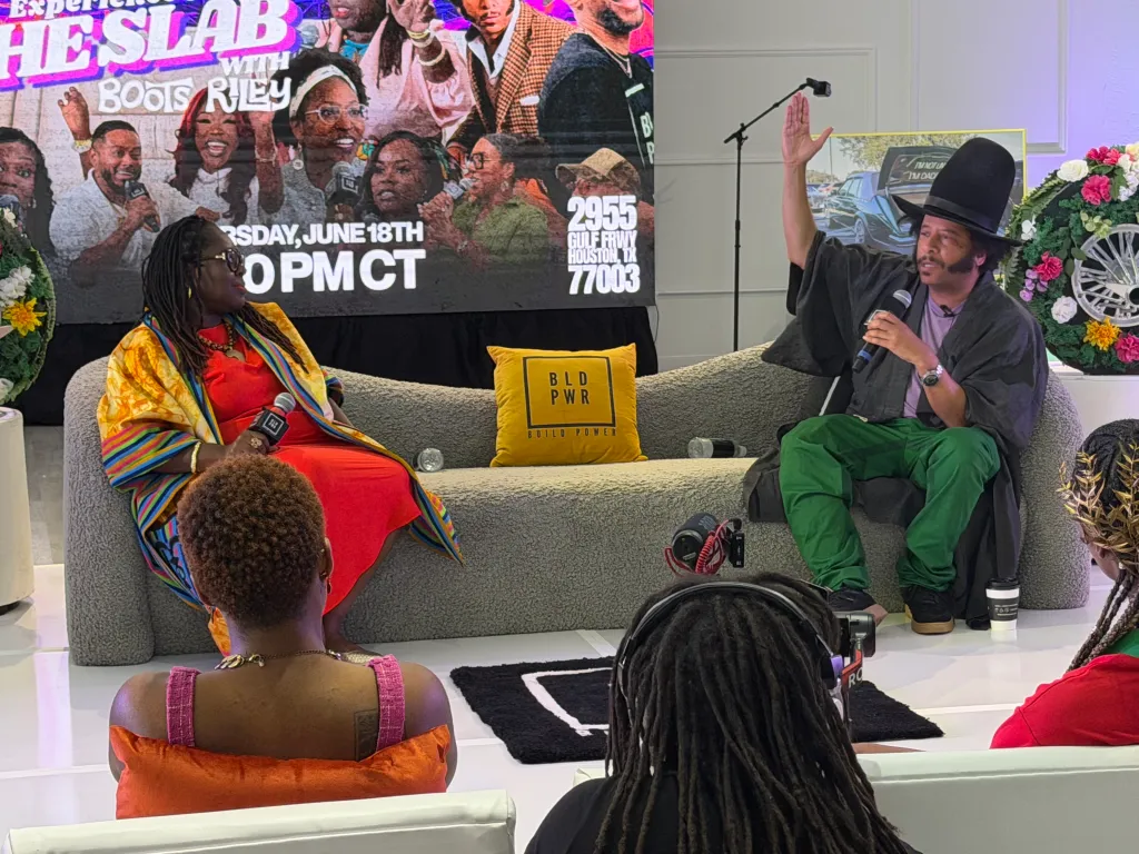 En gruppe mennesker som sitter på en sofa, med en stor begivenhetsplakat i bakgrunnen som annonserer "Experience He Slab" med Boots Riley 18. juni kl. 22.00 CT.