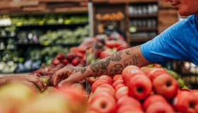 Tatoveret latinomann som strekker seg etter et eple i matvaredelen av en matbutikk