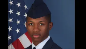 En ung mann i militæruniform står foran et amerikansk flagg.