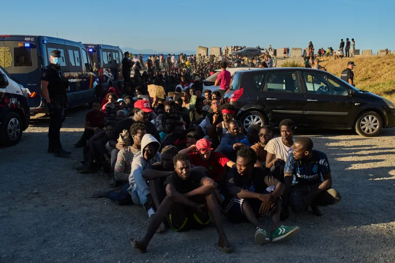 Migranter som krysset fra Marokko til Spania står i kø for matutdeling på en strand i den spanske enklaven Ceuta, mandag 3. august 2026. (AP Photo/Bernat Armangue)