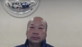 En eldre asiatisk mann iført en marineblå jakke og ser direkte på kameraet.